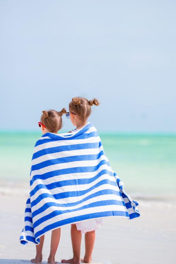 Adorable little girls wrapped in towel at tropical beach after swimming in the sea